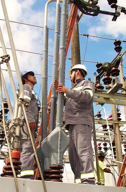 Dois técnicos com uniforme e capacete fazendo manutenção em subestação